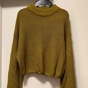 Olivgrön stickad polotröja Divided - Säljer en olivgrön stickad polotröja från Divided. Tröjan har en bred, ribbad krage och är croppad med långa ärmar. Perfekt för dig som gillar chill och avslappnad stil. Materialet är grovstickat och ger en mysig känsla.