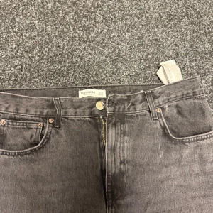 Svarta jeans från Pull&Bear - Säljer ett par svarta jeans från Pull&Bear i klassisk femficksmodell. Jeansen har dragkedja och knapp framtill, samt bälteshällor. Materialet är jeans och färgen är mörk svart, perfekt för en cool och avslappnad look.