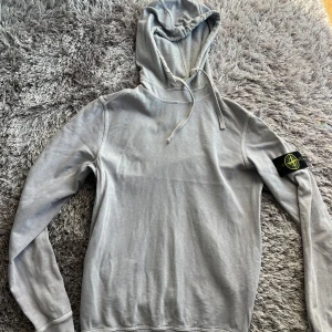 Lila hoodie från Stone Island - Säljer en stilren hoodie från Stone Island med klassisk patch på vänster ärm. Tröjan är ljuslila i verkligheten men ser grå ut på bild.