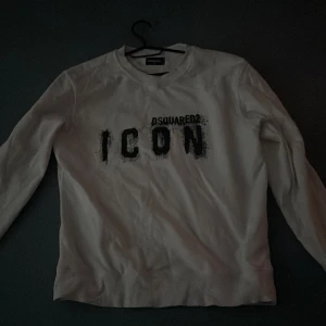 Vit sweatshirt från Dsquared2 ICON - Vit sweatshirt från Dsquared2 i storlek M med svart 'ICON' print på bröstet. Tröjan har rund hals, långa ärmar och ribbade muddar vid hals, ärmslut och nederkant. Snygg och enkel design som sticker ut med den feta loggan framtill.