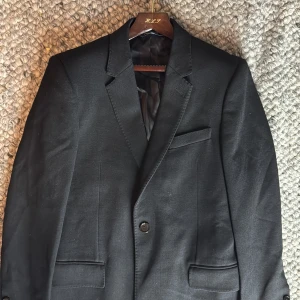 Dolce & Gabbana rock  - Snygg svart rock från Dolce & Gabbana, skräddarsydd i Italien. Klassisk modell med smal passform, två framfickor med lock, bröstficka och knappar vid ärmslut. Fodret är i blankt svart silke som känns lyxigt. Perfekt för dig som gillar stilrena och exklusiva plagg.