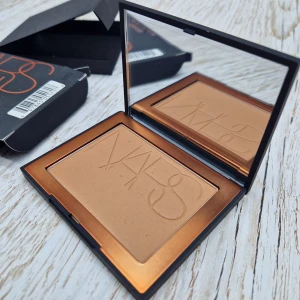 NARS San Juan Bronzer 8g - Bronzing powder från NARS i nyansen San Juan. Kommer i en stilren svart dosa med spegel och orange logga. Pudret har en varm, gyllenbrun ton som ger en naturlig solkysst look. Perfekt för contouring eller att addera glow till ansiktet. Innehåller 8 gram.