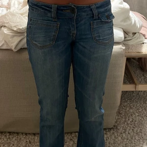 Only lågmidjade jeans - Säljer ett par snygga blå jeans från Only med klassisk femficksdesign och bootcut-ben. Jeansen har låg midja, slitna detaljer och tydliga sömmar. Materialet är robust denim med en cool tvättad look. Perfekt för dig vill ha jeans med lite edge.