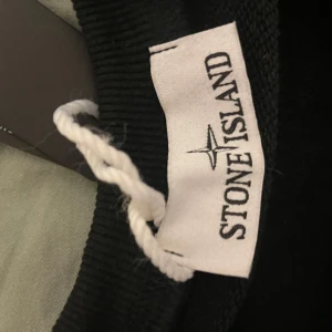 Svart sweatshirt från Stone Island - Svart crewneck sweatshirt från Stone Island med klassisk logotyp-patch på vänster ärm. Tröjan har rund hals, ribbade muddar och är tillverkad i mjuk bomull. Perfekt för dig som gillar stilrena och ikoniska streetwear-plagg.