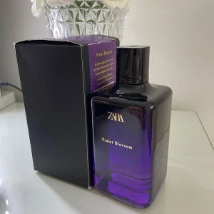 ZARA Violet Blossom parfym 200 ml - ZARA Violet Blossom parfym i en snygg lila och svart glasflaska med guldtext. Doften kommer i en stilren box med lila detaljer och rymmer 200 ml. Perfekt för dig som gillar blommiga och eleganta dofter.