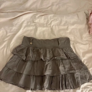 Grå/khaki volangkjol från Madonna - Supersöt grå kortkjol från Madonna i storlek medium. Kjolen har flera lager med volanger och en midja med knappdetalj och snörning. 