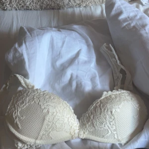 Vit bh intimissimi  - Säljer en vit bh med spetsdetaljer och vadderade kupor. Axelbanden är justerbara och har fina spetskanter. Materialet är mjukt och har en lyxig känsla med broderade blommor över hela framsidan. Använd 1 gång men insåg att den var för liten för mig.