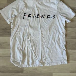 Vit Friends t-shirt  - Säljer en vit t-shirt från H&M med ikoniskt Friends-tryck på bröstet. T-shirten har rund hals, korta ärmar och är gjord i mjuk bomull. Perfekt för dig som älskar tv-serien och vill ha en chill och stilren look.