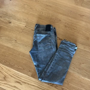 Replay Anbass grå jeans slim fit - Snygga Replay Anbass jeans i grå tvätt med slim fit och klassisk femficksdesign. Jeansen har en modern look med lätt slitningar och smal passform som sitter tajt längs benen. Perfekta för dig som gillar stilrena och bekväma jeans.