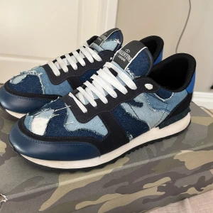 Valentino Garavani Rockrunner denim sneakers - Säljer ett par Valentino Garavani Rockrunner sneakers i storlek 41. Skorna har en cool patchwork-design i olika blå denimtyger med slitna detaljer, svarta och blå mockapartier samt vit snörning. Platt sula och rund tå. Perfekt för dig som gillar statement-sneakers.