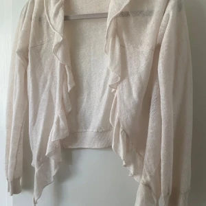  volangkofta - Säljer en creme vit kofta från Rabalder med snygga volangdetaljer längs framkanten. Koftan är stickad, har långärmade ärmar och en öppen design utan knappar. (Är en barnstorlek men passar någon med xxs-xs💕)