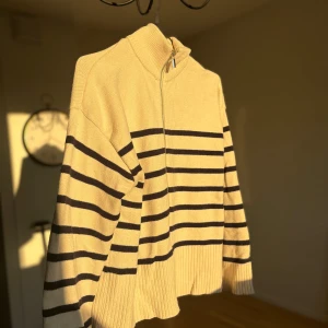 Randig beige  zip tröja från Zara - Beige stickad tröja från Zara i storlek S med mörkblå horisontella ränder. Tröjan har en hög krage, perfekt till hösten och vintern! Ribbad nederkant och ärmslut. Knappt använd, så är i fint skick