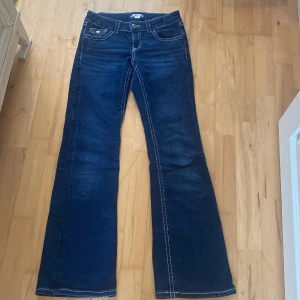 Blå bootcut jeans från Gina Tricot - Snygga mörkblå jeans från Gina Tricot i storlek 158. Modellen har bootcut-ben, klassiska fem fickor och kontrastsömmar. Jeansen är tillverkade i jeansmaterial och har knappar både fram och på bakfickorna för extra detaljer.