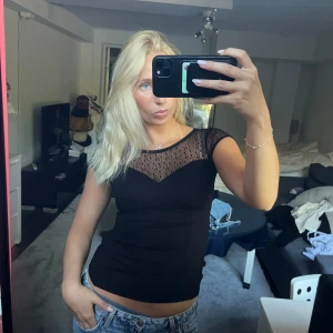 Svart meshblus/spets från Orsay - Supersnygg svart blus från Orsay med mesh/spets upptill och prickigt mönster. Blusen har korta ärmar och en figurnära passform som framhäver siluetten. Detaljer med spets och v-ringad mesh gör den extra cool. Perfekt för utgång bland annat! 