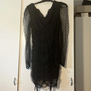 Svart  klänning - Supersnygg svart kort klänning från NA-KD med meshmaterial och prickigt mönster. Klänningen har långa transparenta ärmar, v-ringad hals och cool snörning längst ner. Perfekt för dig som vill sticka ut med en trendig look. Pris kan diskuteras 