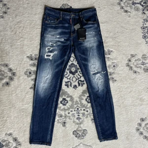 Dsquared2 jeans - Snygga blå jeans från Dsquared2 med slitna detaljer och coola slitningar framtill. Jeansen har fem fickor, klassisk knappgylf och en smal passform. Märkeslapp bak och tydlig Dsquared2-tag vid fickan. Perfekta för en trendig streetstyle.