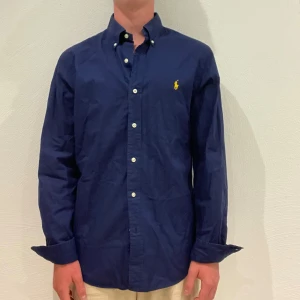 Marinblå Ralph Lauren Skjorta - Marinblå Ralph Lauren skjorta || Storlek M (Slim Fit) || Skjortan är i bra skick || Mitt pris 599kr || Modellen på bilden är 170cm och väger 62kg || Tveka inte på att höra av dig vid frågor eller funderingar 