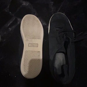 Mörkblå sneakers från Axel Arigato - Snygga mörkblå sneakers från Axel Arigato med vit platt sula och klassisk snörning. Skorna har en rund tå och är tillverkade i mocka för en stilren och modern look. Perfekta för dig som gillar minimalistisk design och vill ha något som funkar till jeans eller shorts.