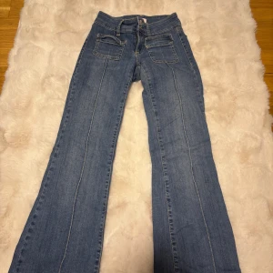 Bootcut jeans från Nelly, blå - Snygga lågmidjade  blå bootcut jeans från Nelly med klassiska fickor fram och bak. Jeansen har ljus tvätt, kontrastsömmar och en låg midja. Materialet är jeans med en mjuk känsla och passformen är loose med utsvängda ben. Perfekta för dig som gillar retrovibbar och avslappnad stil.
