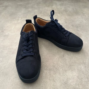 Mörkblå sneakers från Christian Louboutin - Snygga mörkblå sneakers från Christian Louboutin i mocka med klassisk rund tå och platt sula. Skorna har mörkblå snörning och en ikonisk röd gummisula med Louboutin-logga. Insidan är beige och ger en lyxig känsla. Perfekt för dig som gillar exklusiva detaljer. Hör av vid minsta fundering 💫