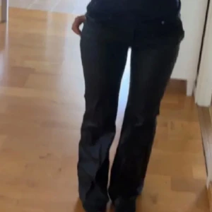 Svarta bootcut byxor i skinnimitation - Snygga svarta byxor från Amsu i skinnimitation med bootcut passform. Byxorna har hällor för bälte och klassisk midja. Nya med prislapp
