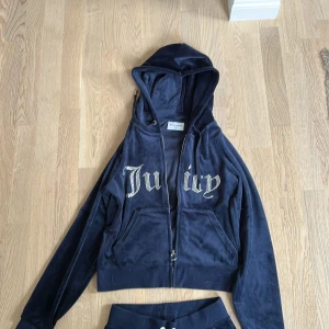 Juicy Couture mörkblå mjukisbyxor och zip up S - Mörkblå mjukisbyxor från Juicy Couture i mjuk sammet med strassdetaljer och broderad JC-logga på fickan. Byxorna har normal passform, raka ben och snörning i midjan. På baksidan finns den ikoniska Juicy-texten i strass. Perfekt för chill och comfy vibes.