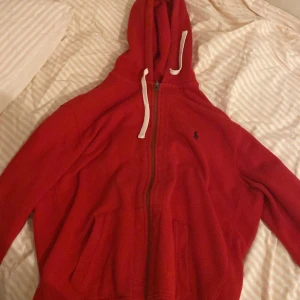 Röd hoodie från Polo Ralph Lauren XL - Säljer en röd hoodie från Polo Ralph Lauren i storlek XL. Tröjan har huva med vita snören, dragkedja framtill och fickor på magen. Klassisk Polo-logga broderad på bröstet. Perfekt för chill dagar och enkel att matcha med jeans eller joggers.
