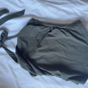 Mörkgrön med knytband top - Säljer en stilren mörkgrön top med knytband i axelband. Toppen har en enkel design och är tillverkad i ett mjukt tyg som känns skönt mot huden. Perfekt för dig som gillar minimalistisk stil.