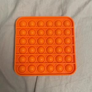Orange pop it-leksak - Säljer en fyrkantig orange pop it-leksak i mjuk silikon. Perfekt för att stressa ner eller bara ha något att pilla med. Den har fem rader med bubblor som kan tryckas in och ut.