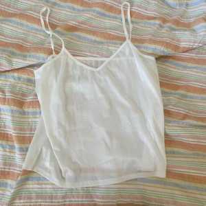 Vit linnetopp med smala axelband - Säljer en enkel och stilren vit linnetopp med smala axelband och v-ringning. Toppen är tunn och luftig, perfekt för varma dagar eller som lager under andra plagg.