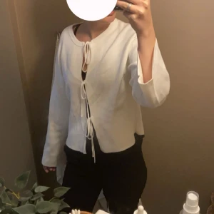 Vit kofta med knyt framtill - Säljer en vit kofta med långa ärmar och knytning framtill. Tröjan har en enkel och stilren design som passar perfekt till många olika outfits. Mjuk och skön att ha på sig.
