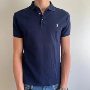 Mörkblå Piké från Polo Ralph Lauren - Säljer en klassisk mörkblå Piké från Polo Ralph Lauren med vit broderad logga på bröstet. Tröjan är i storlek M i slim fit, perekt inför sommaren! 🏖️Tröjan är nästan i nyskick då den endast använts några få gånger! Tveka inte på att höra av dig om du har frågor! 🙌 Priset är inte hugget i sten! 🪨 