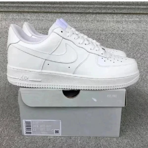 Nike Air Force 1 vita sneakers - Klassiska vita Nike Air Force 1 sneakers med låg profil och rund tå. Skorna har snörning och är tillverkade i skinn med perforerade detaljer på tån för extra ventilation. Perfekta för en clean och stilren look.