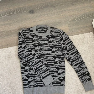 Grå och svart mönstrad tröja från A.P.C. - Säljer en snygg grå och svart stickad tröja från A.P.C. med zebramönster. Tröjan har rund halsringning, långa ärmar och ribbade muddar vid ärmslut och nederkant. Perfekt för dig som vill sticka ut med en cool look. Skick:8/10 Storlek:S 