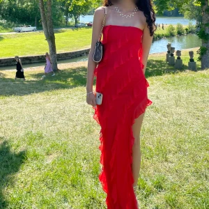 Röd volangklänning med asymmetrisk fåll - Säljer en röd långklänning med volangdetaljer och asymmetrisk fåll. Klänningen är axelbandslös och har en elegant, figurnära passform. Perfekt för bal eller fest. Perfekt till bal eller andra festligheter. Den har en öppning vid benet. Betalade 1200 tillsammans med tull och frakt. Endast använd en gång 