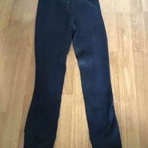 Svarta ridbyxor från CRW - Svarta ridbyxor från CRW med helskodd silikongrepp längs insidan av benen och sätet. Byxorna har en klassisk passform och är perfekta för ridning. Elastisk midja med CRW-logga och förstärkta detaljer för extra hållbarhet.