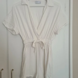 Vit playsuit från Bershka - Säljer en vit playsuitfrån Bershka i storlek XS. Den har korta ärmar, krage, knyt i midjan och v-ringad hals. 