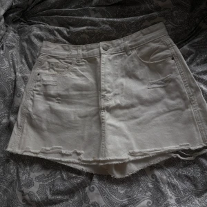 Vit jeanskjol från PNK W - Storlek 38/ w28. En vit jeanskjol från PNK W i modell skort, med råa kanter och slitna detaljer framtill, kjolen har även inbyggda shorts. Kjolen har klassiska fickor både fram och bak samt knapp och dragkedja i midjan. Perfekt för en avslappnad och trendig look. Behöver tyvärr sälja mina två favoritkjolar då jag gått ner i vikt och dom inte passar längre (säljer en ljusblå också)