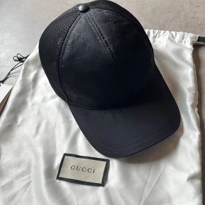 Svart keps från Gucci - Säljer pga ej använd på ett tag, skick 9/10 och allt på bilder medföljer. Påse, lappar etc. Inköpt ifrån haiendo.shop för ett tag sedan! Snygg svart keps från Gucci med diskret GG-mönster på framsidan och mesh baktill för extra ventilation. Justerbar passform med plastspänne. Perfekt för en stilren och trendig look. (Storlek M) Nypris 3000-4000kr.