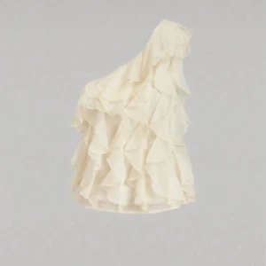 Vit volangklänning med oneshoulder - Säljer en superfin vit klänning med volanger och oneshoulder-design. Klänningen har en asymmetrisk axel och flera lager av volanger som ger en riktigt snygg och unik look. Perfekt för dig som vill sticka ut!