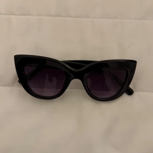 Svarta cat eye-solglasögon - Snygga svarta solglasögon i cat eye-modell med mörka glas. Ramen är kraftig och ger en cool retrovibe. Perfekta för att lyfta vilken outfit som helst.