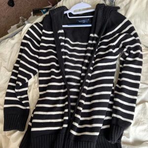 Svartvit randig stickad kofta  - Säljer en svart och vit randig stickad kofta. Koftan har långa ärmar och bred ribbad krage. Perfekt för lager-på-lager och passar till många olika outfits. Har en fläck på ena armen som syns på en av bilderna.