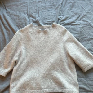 Beige stickad tröja från & Other Stories - Mysig beige stickad tröja från & Other Stories Stockholm Atelier. Tröjan har rund halsringning och trekvartsärm, perfekt för lager-på-lager. Enkel och stilren design som passar till mycket.