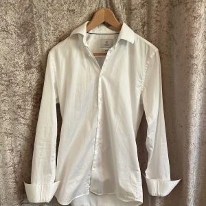 Vit skjorta från Bläck - Klassisk vit skjorta från Bläck med slim fit-passform. Skjortan har långa ärmar, knappar framtill och en stilren krage. Perfekt för dig som gillar en enkel och stilren look. Skick 9,5/10, användes 1 kväll och sen dess har den inte kommit till användning. Storlek XS!! Perfekt under kavaj eller över T-shirt. Nypris 1200 kr 