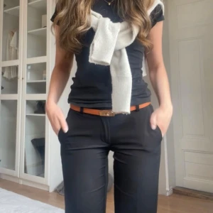 Svarta kostymbyxor med bootcut - Snygga svarta kostymbyxor med bootcut passform och normal midja. Byxorna har bälteshällor och klassiska fickor, perfekta för en stilren look. Materialet känns mjukt och följsamt, och de passar till många olika outfits.