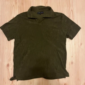 Olivgrön frotté t-shirt från S.C.W. - Säljer en olivgrön t-shirt från S.C.W. i mjuk frotté med kort ärm och klassisk krage. T-shirten har en bröstficka och avslappnad passform, perfekt för en chill stil till sommaren.