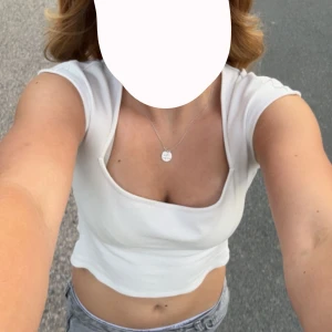 Vit croppad topp med kort ärm - Säljer en vit croppad topp med korta ärmar och rund halsringning. Toppen har en tight passform och är perfekt för varma dagar. Enkel och stilren design som passar till mycket.