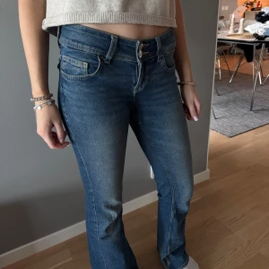 Blå bootcut jeans med låg midja - Snygga blå jeans med bootcut passform och låg midja. Klassisk femficksmodell med dragkedja och knapp framtill. Jeansen har en lätt tvättad look och är perfekta för en avslappnad stil. Lite slitna baktill men inget som syns tydligt .🥰
