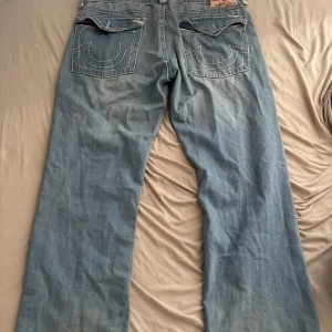 True Religion ljusblå jeans  - Säljer ett par ljusblå jeans från True Religion med klassiska vita kontrastsömmar och detaljerade bakfickor. 