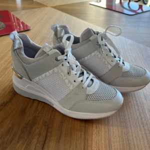 Sneakers från Michael Kors - Säljer dessa snygga grå/vita sneakers från Michael Kors med silvriga detaljer och meshpartier på sidorna. Skorna är rejält upphöjda i sulan likt Isabel Marant skorna. OBS: det är inte en fläck på sidan utan skuggbilderna på mockatycket. Endast använd på test 1 timme - därför så ren sula. Finns en liten defekt pga att skon kommit åt något (be om bildj Nypris: 2195!!